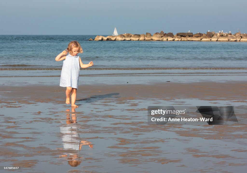 Toddler and her reflection on sandy beach