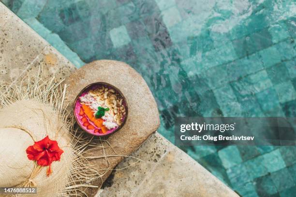 tropical background. top view of fruit smoothie bowl and straw hat on poolsige - bordo piscina foto e immagini stock
