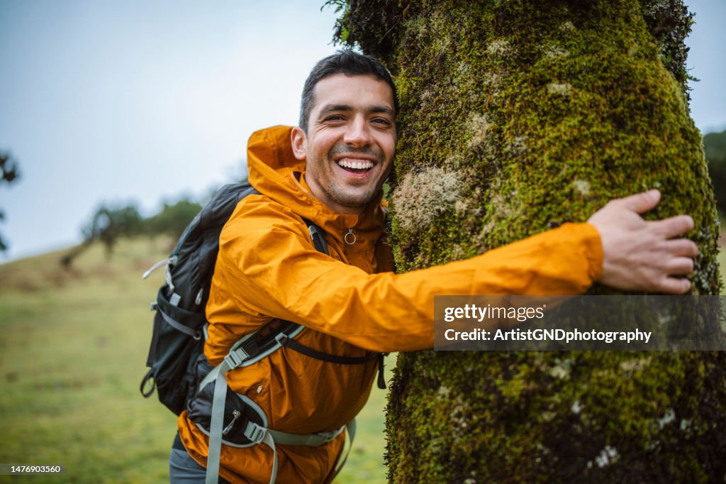 Smiling man embracing a tree in nature.