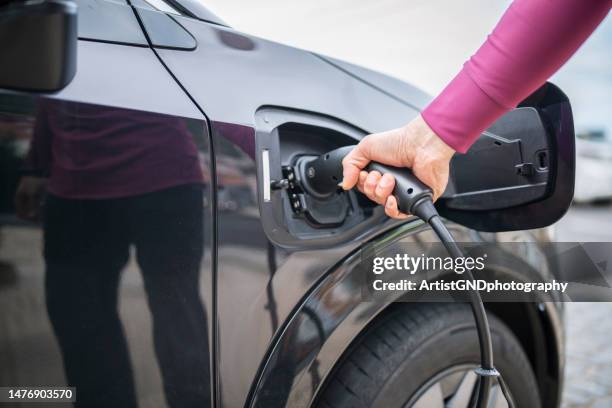 midsection of man plugging cable in electric car. - cladding stockfoto's en -beelden