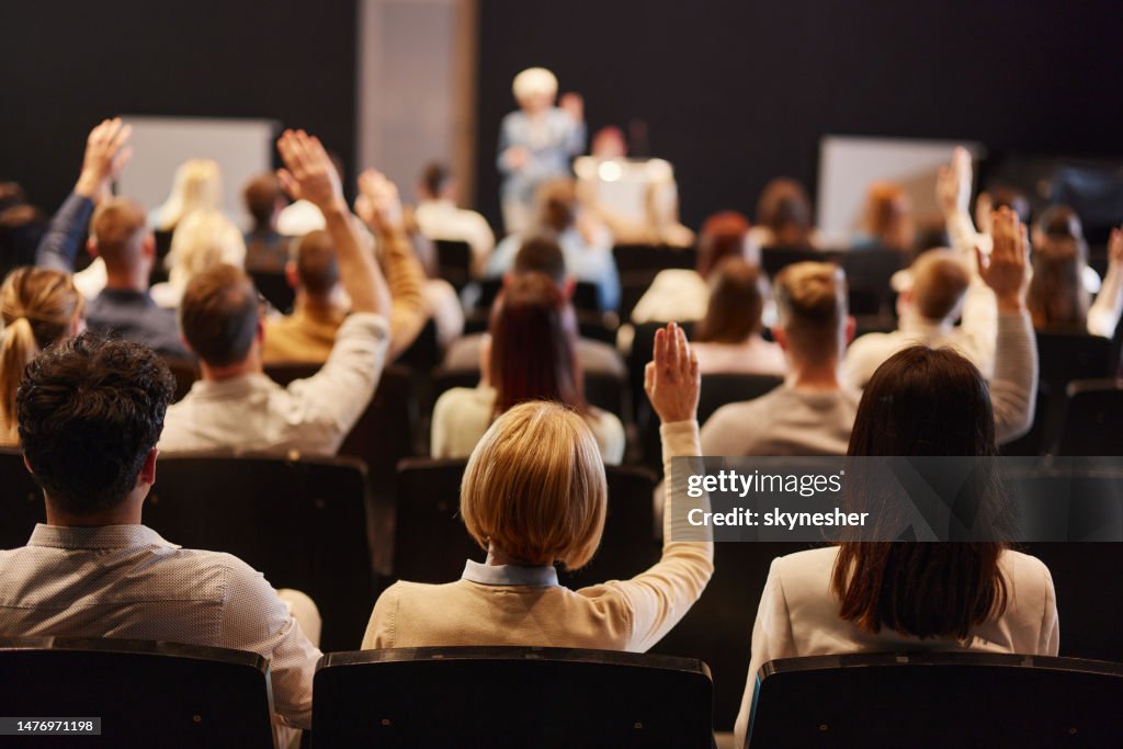 Rückansicht einer Menschenmenge, die bei einem Seminar im Kongresszentrum die Hände hebt.