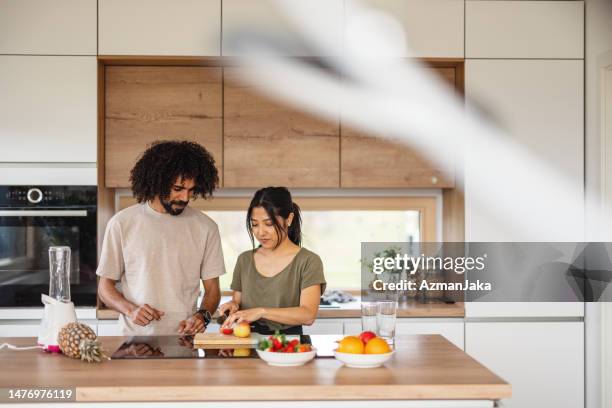 家で健康的なスムージーを準備する恋をしている陽気な多民族夫婦 - middle aged couple cooking ストックフォトと画像