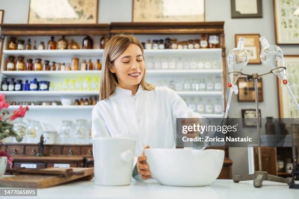 female pharmacist working in drugstore preparing herbal medicine in mortar bowl - mortar and pestle stock pictures, royalty-free photos & images
