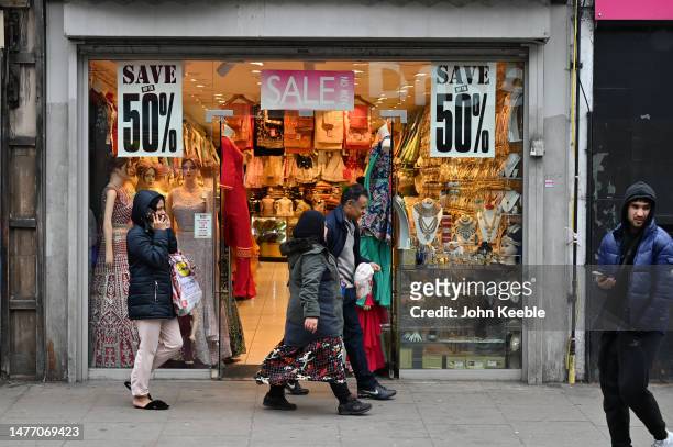 People walk past a fashion shop advertising a 50% sale selling sarees, lehengas and bridal jewellery in Upton Park Green Street on March 23, 2023 in...