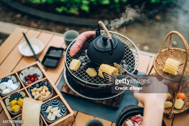 cropped shot of a female hand grilling sweet corn and vegetables with a pot of tea during barbecue party, having a relaxing time and enjoying a slow life in the garden. outdoor fun. healthy eating. people, food and lifestyle - chinese eating backyard stock pictures, royalty-free photos & images