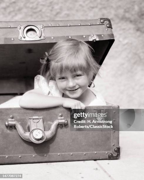 1930s girl peeking out from a suitcase trunk smiling looking at camera.