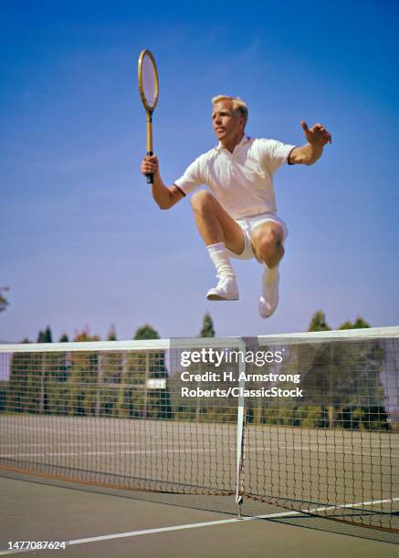 1960s Male tennis player jumping over net.