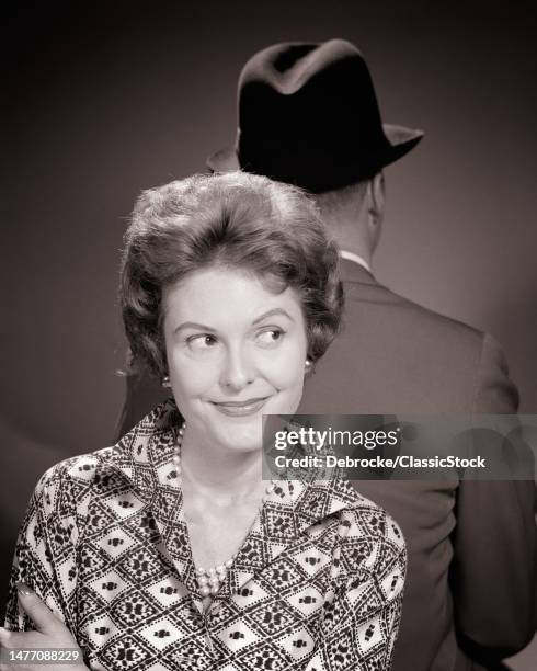 1950s woman wife or secretary looking slyly off to the side standing back to back with a businessman her boss or her husband.