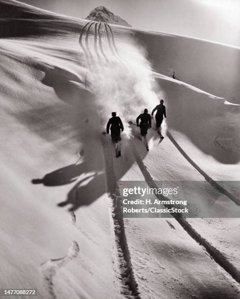 1950s three anonymous silhouetted men skiing downhill in the Swiss Alps making tracks and casting shadows.