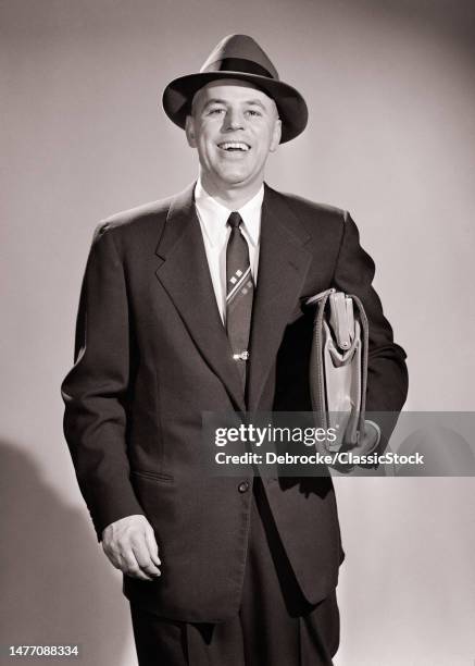 1950s smiling salesman looking at camera wearing business suit holding briefcase under his arm.