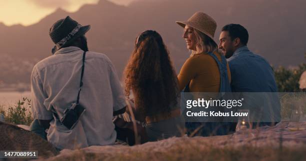 sunset, calm and back of friends in nature for travel, celebration and bonding. summer break, picnic and party with group of people talking in outdoors for mountains view, happiness and holiday - picnic rug stockfoto's en -beelden