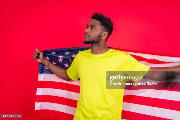 portrait of smiling african american man holding usa flag, cheerful black man looking at camera proudly isolated on red background, celebrating independence day, 4th of july - classic day 4 stock pictures, royalty-free photos & images