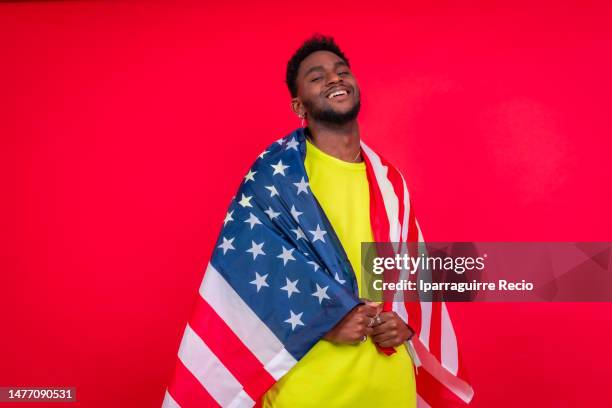 young african american man smiling with usa flag, cheerful black man looking at camera proudly isolated on red background, celebrating independence day, 4th of july - classic day 4 stock pictures, royalty-free photos & images