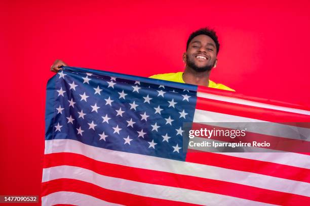 portrait of smiling african american man holding usa flag, cheerful black man looking at camera proudly isolated on red background, celebrating independence day, 4th of july - classic day 4 stock pictures, royalty-free photos & images