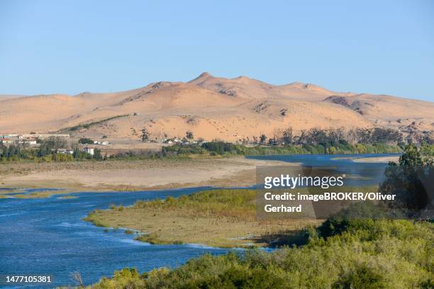 orange river, also known as the orange river, on the border between namibia and south africa, sand dunes behind, oranjemund, sperrgebiet national park, also known as tsau ǁkhaeb national park, namibia - south namibia stock pictures, royalty-free photos & images
