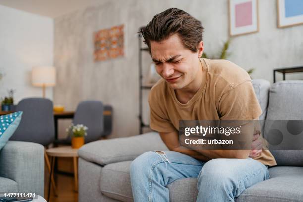 young man having stomach pain at home - male stomach stock pictures, royalty-free photos & images