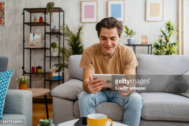 young man using tablet at home - how to upload photos stock pictures, royalty-free photos & images