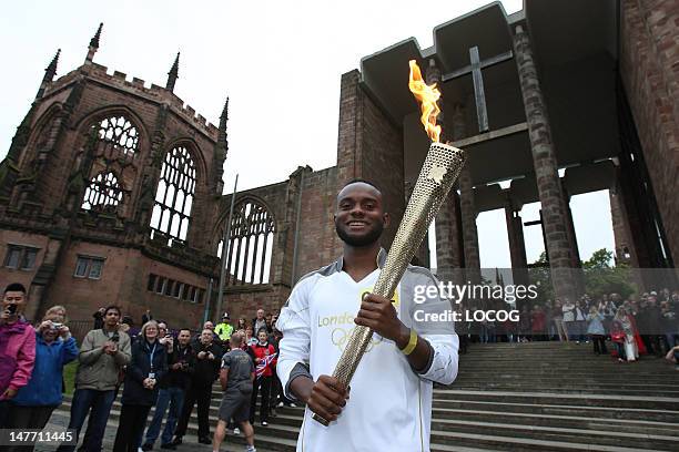 In this handout image provided by LOCOG, Torchbearer Torchbearer 002 Ali Abdillahi holds the Olympic Flame at the Coventry Cathedral ruins during day...