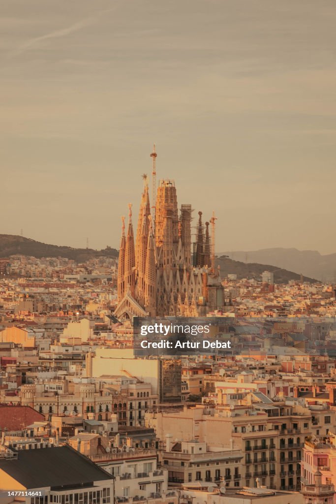 The Sagrada Familia emerging from the Barcelona city with the Eixample neighborhood rooftops and golden light.
