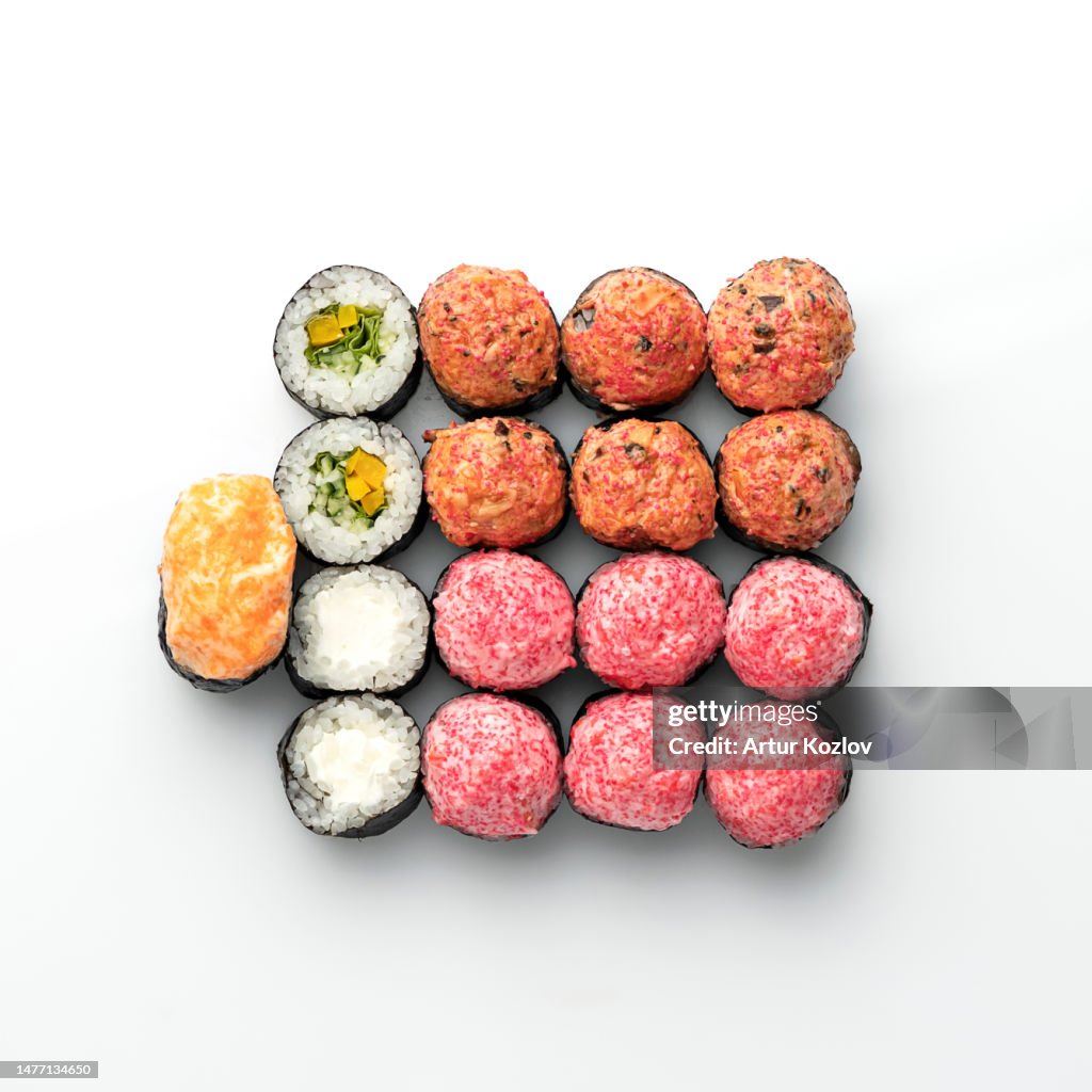 Large set of baked sushi rolls with different fillings, decorated with tobiko caviar mousse.. Japanese, Asian cuisine. Seafood dish. White background. View from above. Soft focus. Copy space