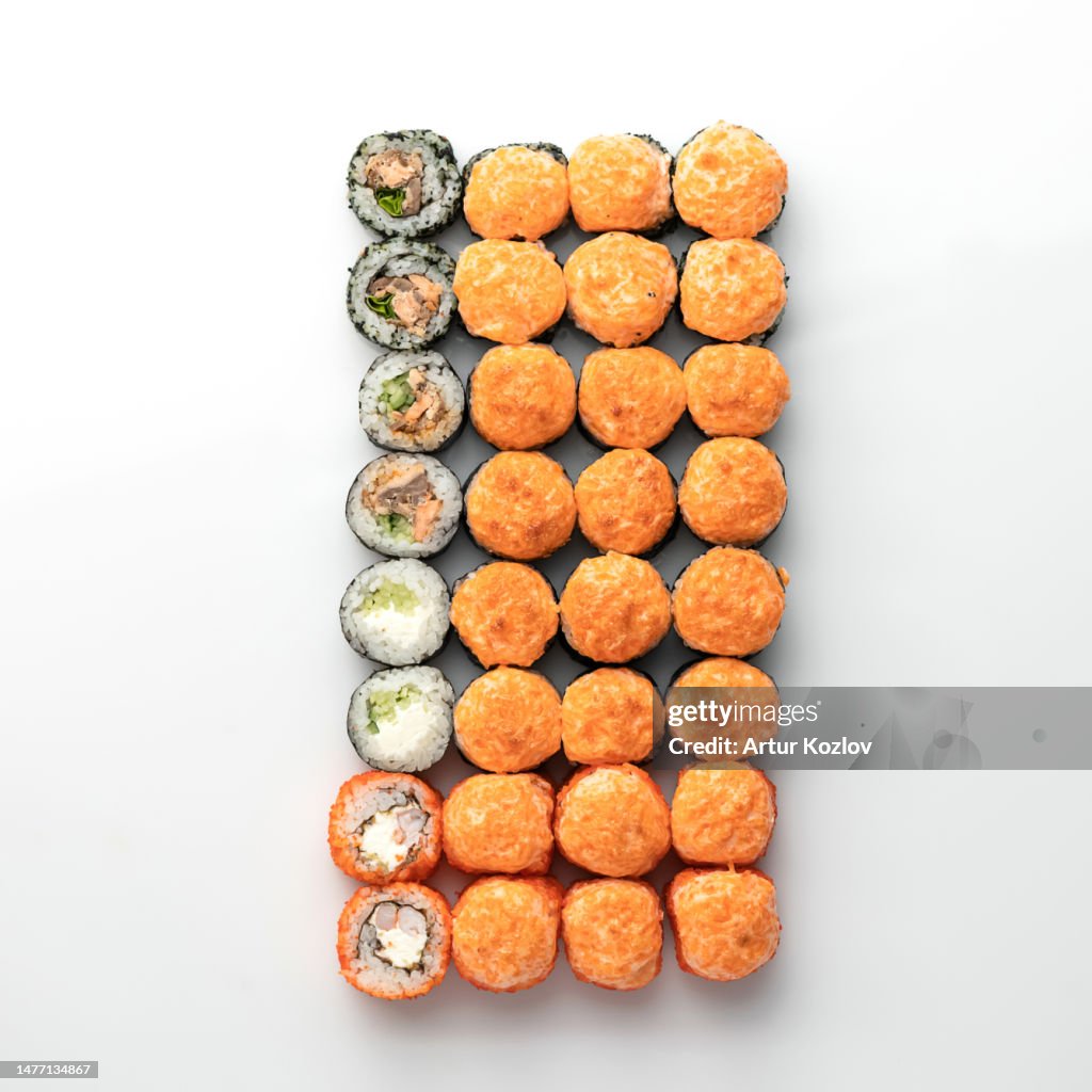 Large set of baked sushi rolls with different fillings, decorated with tobiko caviar mousse.. Japanese, Asian cuisine. Seafood dish. White background. View from above. Soft focus. Copy space