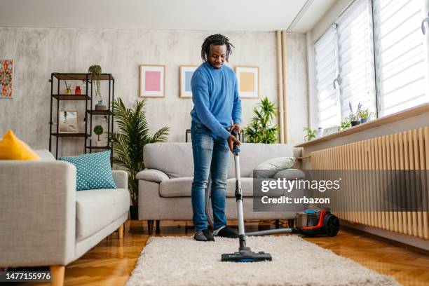 young man vacuuming the carpet in his apartment - stofzuiger stockfoto's en -beelden