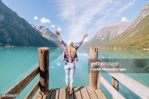 friedliche frau, die sich auf einem hölzernen pier über dem schönen see entspannt, sie öffnet ihre arme weit und umarmt die reine natur - open arms stock-fotos und bilder