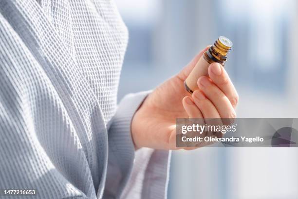 woman in bathrobe holds essential oil on hand. - brown bottle stock pictures, royalty-free photos & images