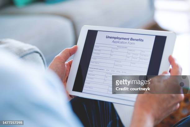 man looking at an unemployment benefits form on a digital tablet. - unemployment benefits stock pictures, royalty-free photos & images