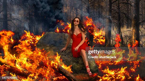 woman in a red dress sitting on a rock in a burning forest - photoshop photos et images de collection