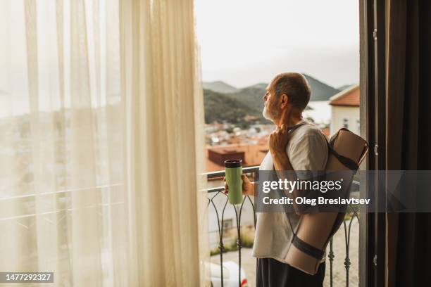 senior man on balcony in morning, with rolled mat and water bottle, ready to yoga practicing. - good morning stock pictures, royalty-free photos & images