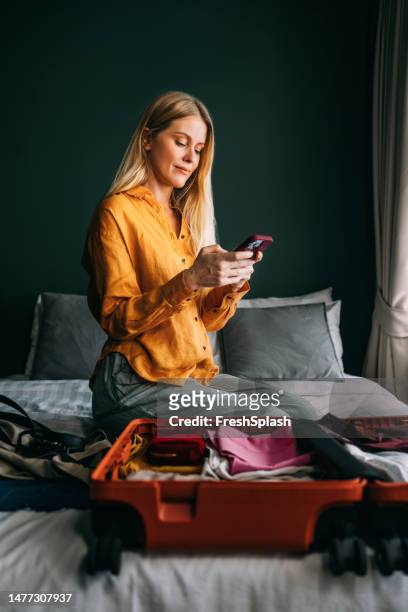 una bella donna d'affari bionda felice che invia messaggi sul suo cellulare mentre prepara la valigia per un viaggio d'affari - businesswoman blond looking left foto e immagini stock