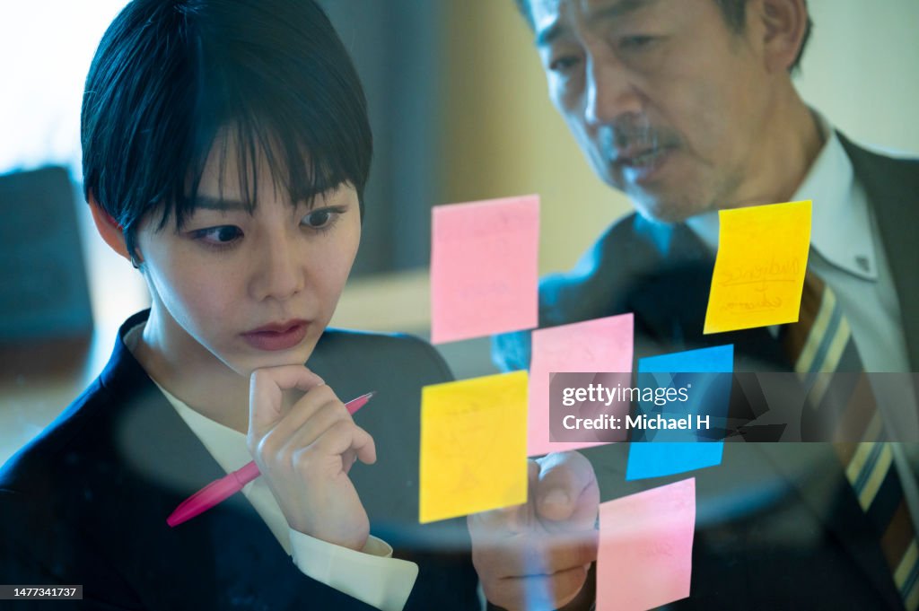 Business people brainstorming strategy and new ideas on glass wall with adhesive notes