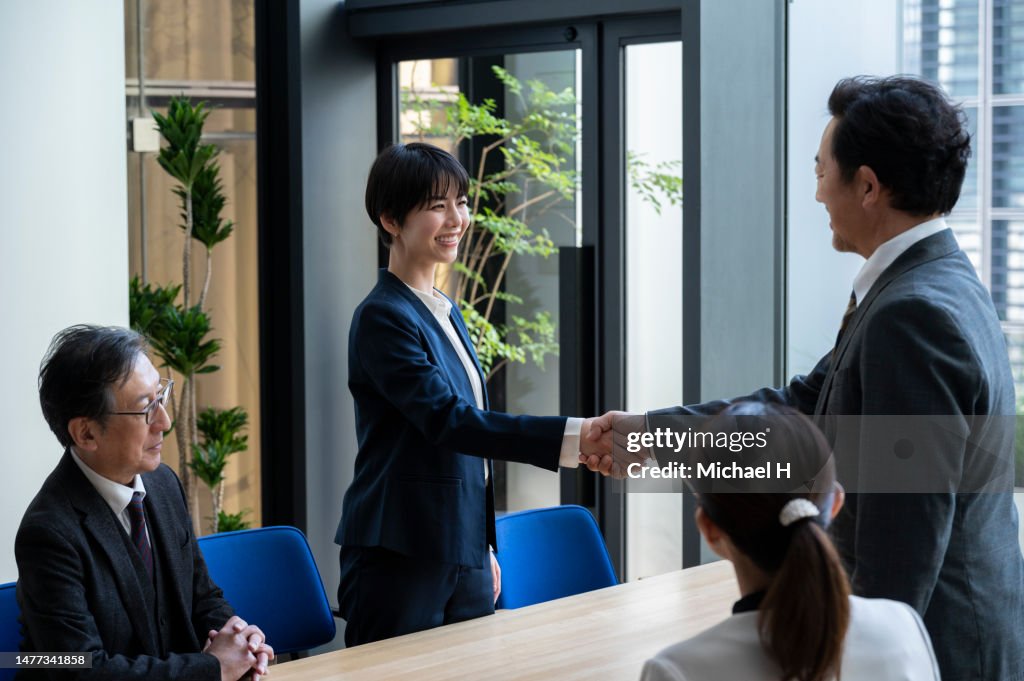 A woman smiling and shaking hands after a business deal is concluded.