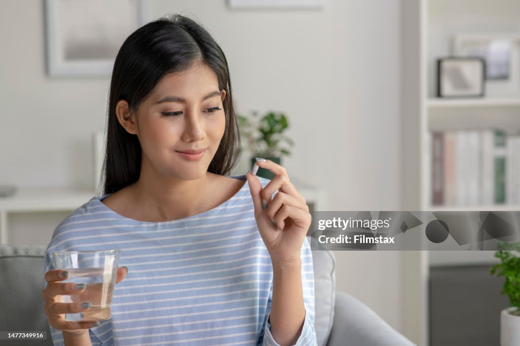 Giovane donna asiatica che prende pillola e vitamina nel soggiorno