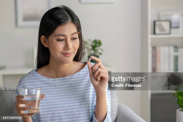 young asian woman taking pill and vitamin in the living room - vitamin stock pictures, royalty-free photos & images