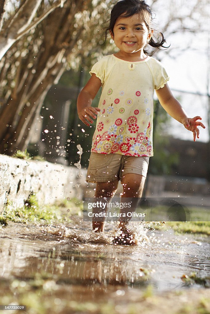 Toddler girl running through muddy water