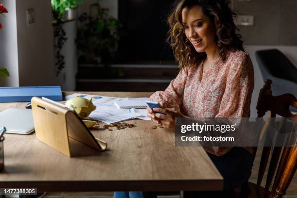 young woman counting coins from a broken piggy bank and using calculator - broken calculator stock pictures, royalty-free photos & images