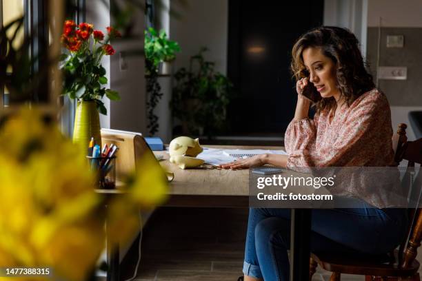 young woman talking on the phone with her bank while counting coins and calculating savings - broken calculator stock pictures, royalty-free photos & images