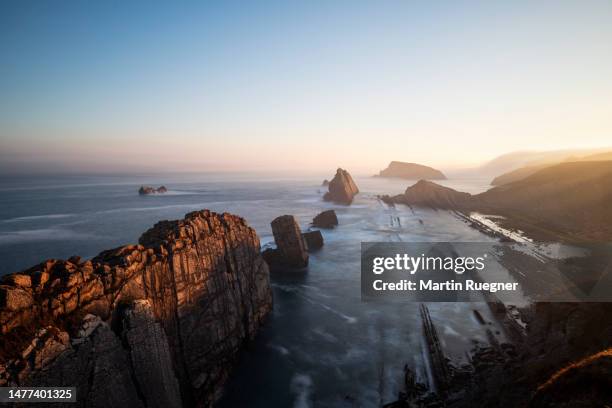 surf on the rocks at playa de la arnia beach at sunrise, near liencres. this area is called costa quebrada. playa de la arnia, bay of biscay, liencres, santander, costa quebrada, cantabria, spain, atlantic ocean. - force de la nature stock pictures, royalty-free photos & images