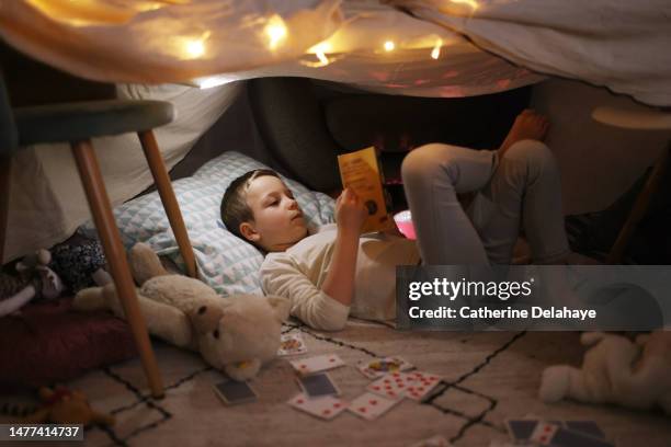 a little boy reading in a homemade illuminated hut, at home - cabane photos et images de collection