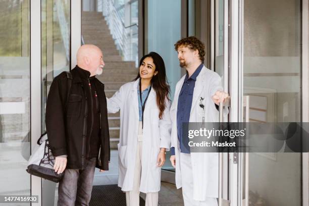 smiling doctors looking at senior male patient with bag outside hospital - hospital doorway stock pictures, royalty-free photos & images