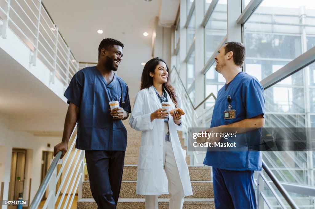 Happy multiracial healthcare workers talking while standing on staircase at hospital