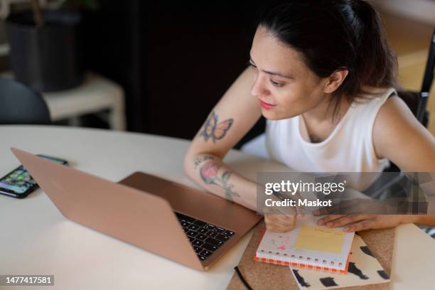 woman with paraplegia writing in diary while looking at laptop - dining table icon stock pictures, royalty-free photos & images