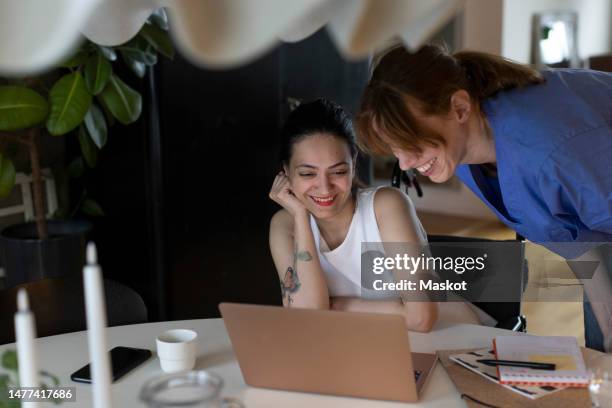 nurse and woman with paraplegia watching laptop together at home - dining table icon stock pictures, royalty-free photos & images