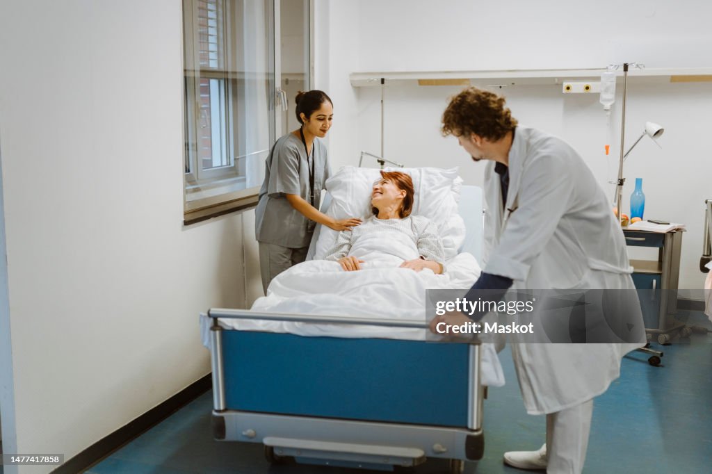 Smiling female senior patient lying on bed amidst healthcare workers at hospital