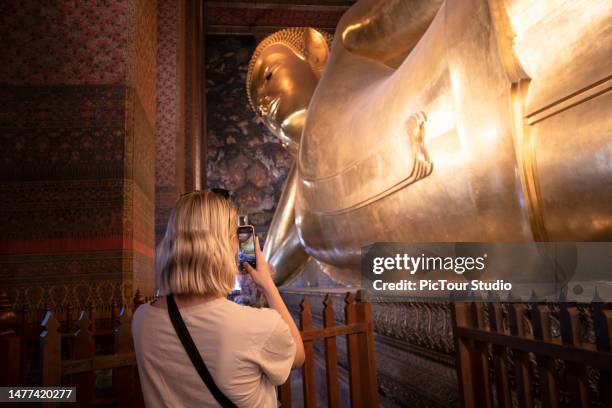 women taking picture of golden reclining buddha statue at wat pho in bangkok thailand - buddha face stock pictures, royalty-free photos & images