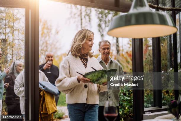 senior woman walking with food bowl during dinner party - group of mature men stock pictures, royalty-free photos & images
