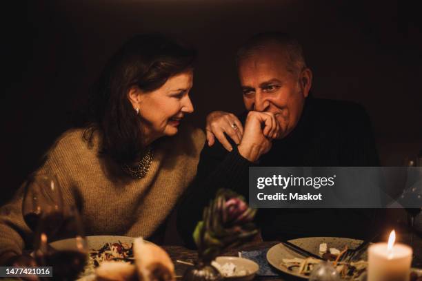 smiling senior woman talking to mature man with hand on chin at dinner party - kerzenschein stock-fotos und bilder
