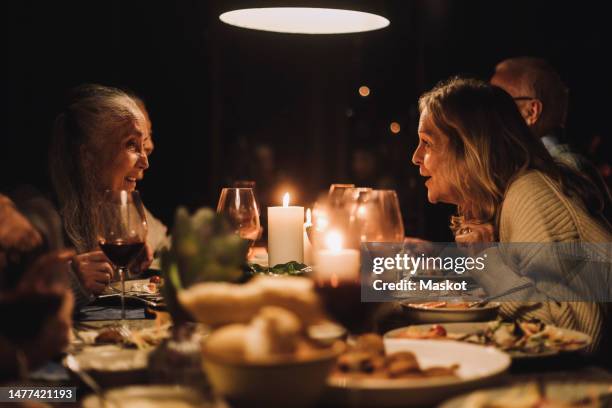 senior woman talking to female friend at dining table during candlelight dinner party - kaarslicht stockfoto's en -beelden